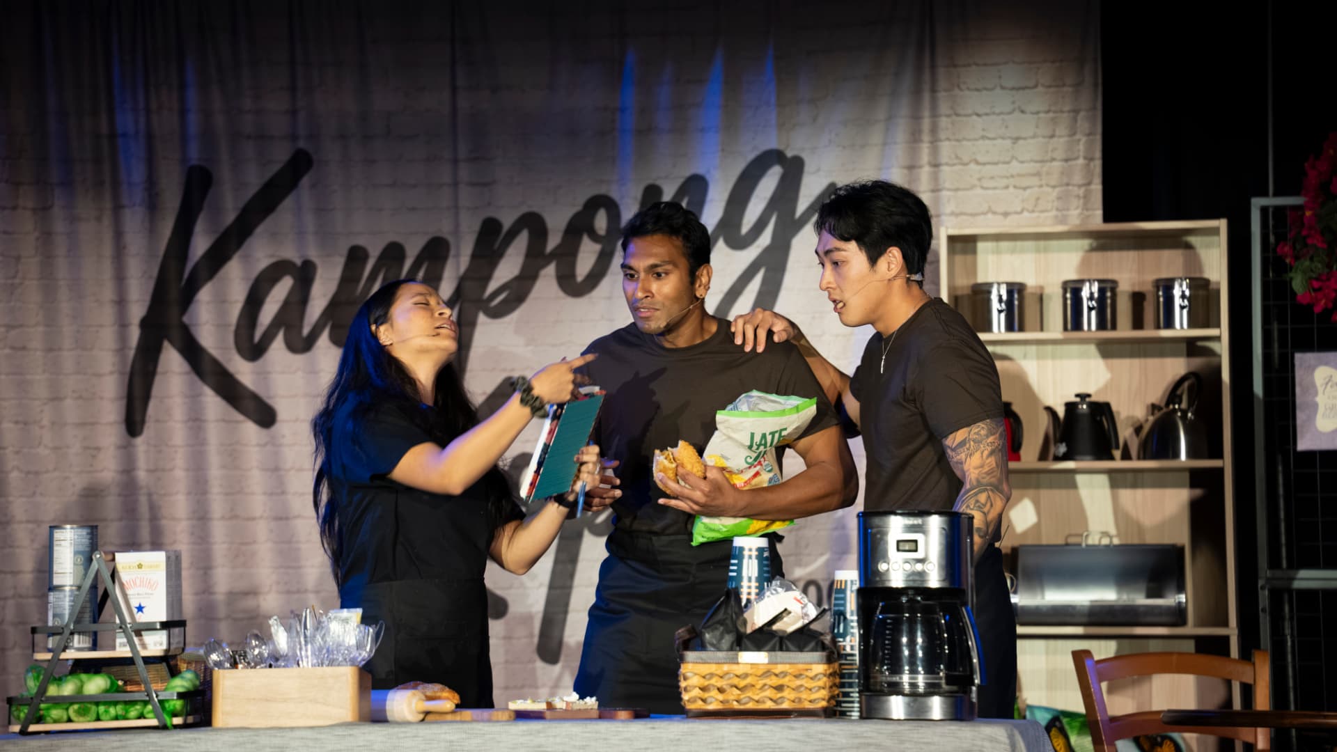 Kampong Kopi, USA — three performers share a tense, tender moment on the kopitiam set